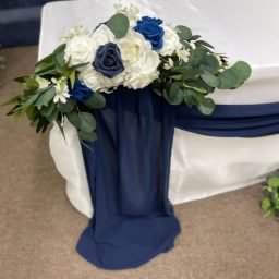 Floral arrangement on B&G table Floral arrangement with blue and white flowers draped over a navy fabric.